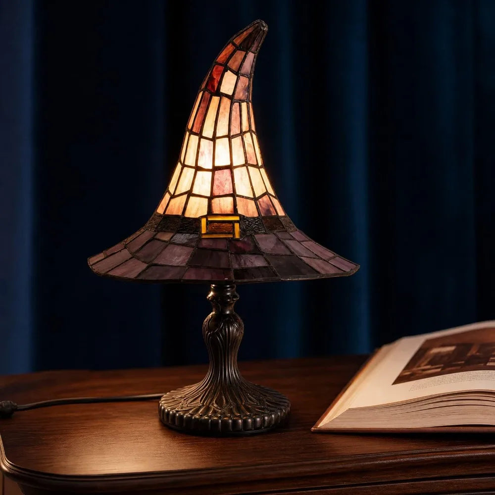 Witch hat lamp lit on a desk next to an open book, dark blue curtains behind